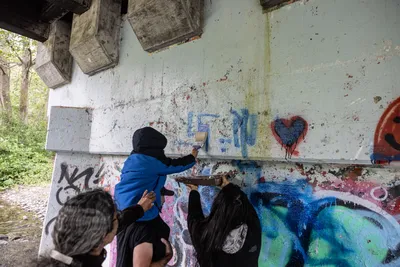 Friends including Jay Lundahl (painting with extension roller), Theresa Churchill (looking up), and others gather under a bridge to paint over hateful graffiti in Sequim, Washington on June 17, 2023.